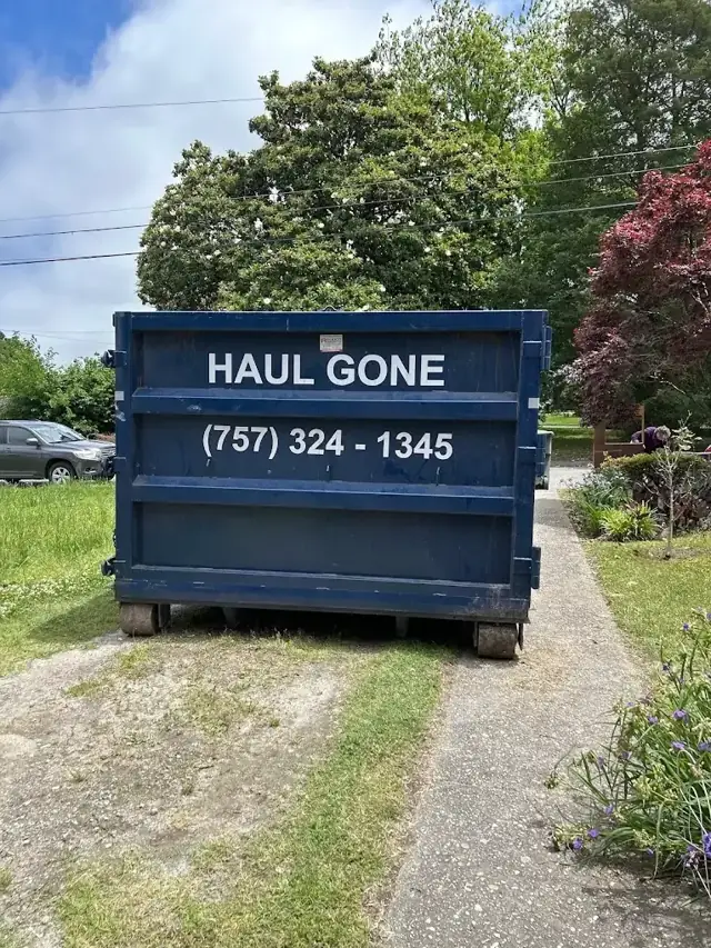 Navy Haul Gone roll-off dumpster set at the end of a residential driveway