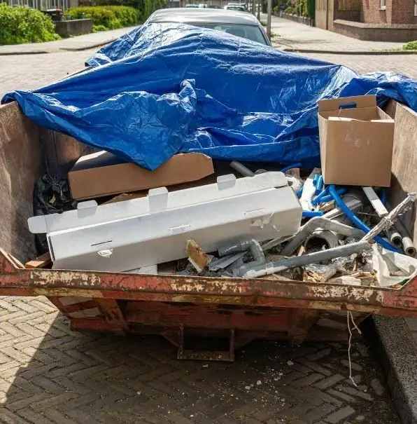 Roll-off dumpster loaded with fixtures and cardboard under a blue tarp