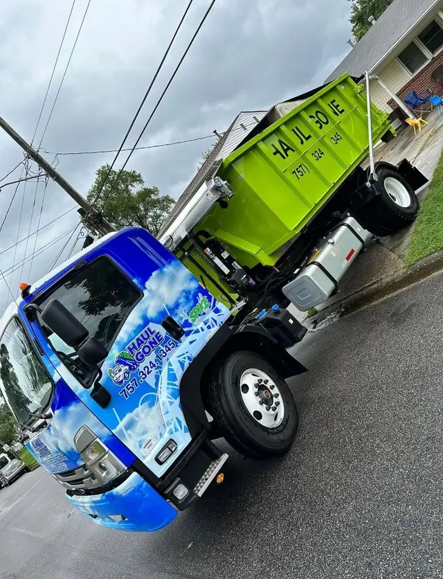 Wrapped Haul Gone box truck carrying a green roll-off on a residential street